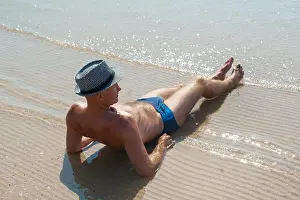 Surfer Prints: Stylish young male model man lying on beach sand wearing hipster summer hat enjoying summer travel holiday near the sea