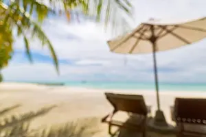 Summer exotic sandy beach with blur palms and sea on background. Dream vacation background with palm leaves and sea view. Summer paradise island beach