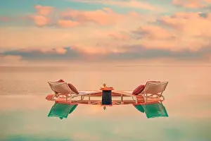 Summer love and romance table setup for a romantic dinner meal with luxury infinity pool reflection chairs under sunset sky and sea in background