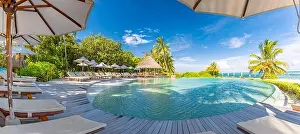 Summer outdoor tourism landscape. Luxurious beach resort with swimming pool and beach chairs or loungers under umbrellas with palm trees and blue sky