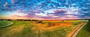 Summer rural sunset aerial panorama. Wheat agricultural fields on hills. Road to village, Belarus