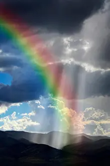 Rising Prints: Sunlight rays from clouds falling on dark mountain range with Rainbow