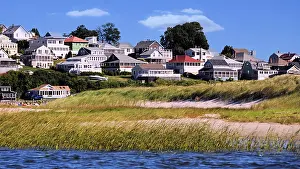 Blue Skies Prints: Sunlight scene of many homes and cottages on a hillside overlooking sand and grass dunes and sparkling blue ocean