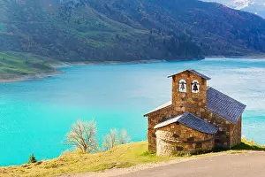 Sunny picturesque view of stone chapel on Roselend lake (Lac de Roselend) in France Alps (Auvergne-Rhone-Alpes). Landscape photography