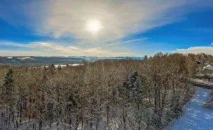 Sunny winter day in aerial view over the tree tops to the alp mountains in the winter background