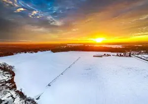Sunrise at the farm with irrigation equipment on frozen field and barn house
