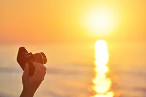 Sunrise over the sea coast. Fireball of the sun above the horizon in a colorful orange sky. Vintage SLR camera in hand in the foreground