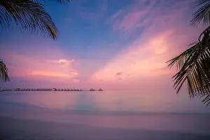 Sunset on Maldives island, luxury water villas resort. Beautiful sky and clouds and palm leaves beach background for summer vacation holiday
