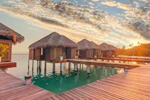 Sunset on Maldives island, luxury water villas resort hotel and wooden pier. Colorful sky and clouds and beach background for summer vacation holiday