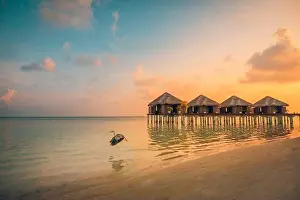 Sunset on Maldives island, luxury water villas resort and wooden pier. Beautiful sky clouds and beach background for summer vacation holiday travel