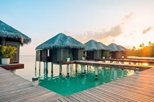 Sunset on Maldives island, luxury water villas resort and wooden pier. Beautiful sky clouds and beach background for summer vacation holiday travel