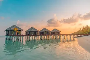 Sunset on Maldives island, luxury water villas resort and wooden pier. Beautiful sky clouds and beach background for summer vacation holiday travel
