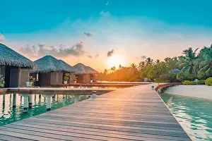Sunset on Maldives island, luxury water villas resort and wooden pier. Beautiful sky clouds and beach background for summer vacation holiday travel