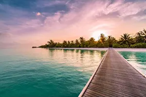 Sunset on Maldives island, luxury water villas resort and wooden pier, palm tree beautiful sky and clouds beach background for summer vacation holiday
