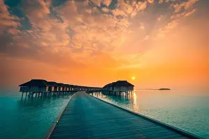 Sunset on Maldives island, luxury water villas resort and wooden pier. Beautiful sky and clouds and beach background for summer vacation holiday