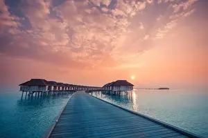 Sunset on Maldives island, luxury water villas resort and wooden pier. Beautiful sky and clouds and beach background for summer vacation holiday