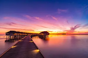 Sunset on Maldives island, luxury water villas resort and wooden pier. Beautiful sky and clouds and beach background for summer vacation holiday