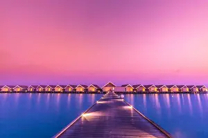 Sunset on Maldives island, luxury water villas resort and wooden pier. Beautiful sky and clouds and beach background for summer vacation holiday