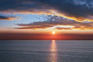 Sunset in the ocean with large sun dusk soft waves and red cloudy sky. Sea sunrise background. Landscape photography
