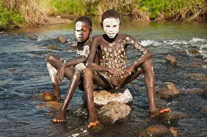 Two Surma boys with body paintings sitting on a rock in the river, Kibish, Omo River Valley, Ethiopia