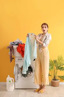 Hygienic Prints: Surprised young woman with dirty laundry near washing machine on yellow background