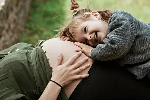 Prenatal Prints: A sweet moment as a young girl with a big smile listens to a pregnant belly