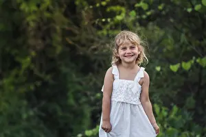 Blonde Prints: Sweet smiling 4 yr old girl in white sundress with backdrop of foliage
