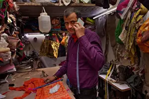 Indian Culture Prints: Tailor talking on mobile phone while working in his workshop