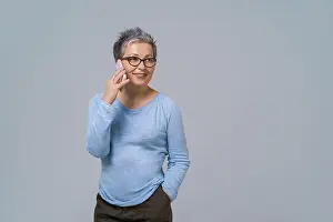 Senior Women Prints: Talking on the phone mature grey hair woman in glasses turn sideways holding smartphone in her hand wearing blue blouse