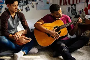 Hangout Prints: Teenage boys hanging out in a bedroom playing an acoustic guitar hobby and music concept