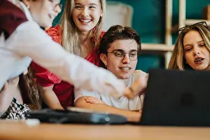 Informal Prints: Teenage friends collaborating and smiling while gathered around a laptop in a casual group study