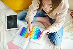 Flexible Prints: Teenage girl playing with rainbow pop-it fidget toy while studying at home