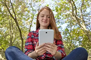 Texting Prints: A teenage girl wearing jeans and a plaid shirt sits on a boulder using her smart phone