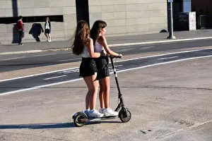 Two teenage girls riding together an electric scooter in a street of a city