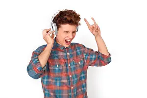 Homosexual Prints: Teenager boy wearing wireless headphones studio standing isolated on white wall listening rock music showing horns