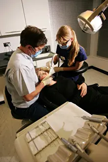 Dentistry Prints: Teeth and gum treatment by a dentist and his assistant on a patient in a dentists chair in a dental surgery