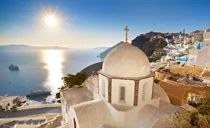 Thira (capital city of Santorini) - greek white church overlooking the sea and sun on blue sky, Santorini Island, Greece