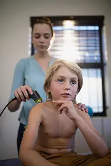 Low Section Prints: Thoughtful shirtless boy sitting with female therapist using ultrasound machine on shoulder at hospital ward