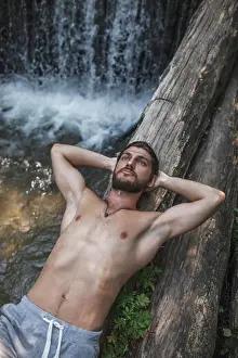 Weekend Activities Prints: Thoughtful shirtless man lying on logs over waterfall at forest