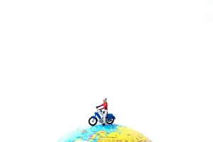 Stunt Prints: Tiny miniature model of the man is riding the motorbike or motorcycle on globe using as travelling
