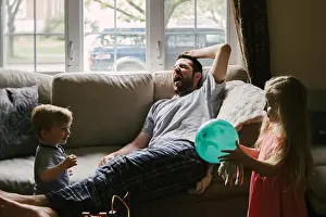 Pajamas Prints: A tired father lies on the couch while his children play around him