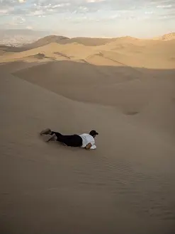 Snowboard Prints: Tourist sliding down slopes of Huacahina sand dunes on snowboard sandboarding adventure adrenaline fun extreme sports