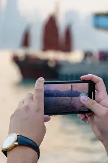 Taking Photo Prints: Tourist taking a photo on her mobile phone of the Hong Kong skyline at sunset
