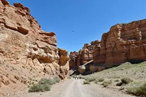 Cavern Prints: Tourists travel along the bottom of a deep warn colored canyon accompanied by a drone