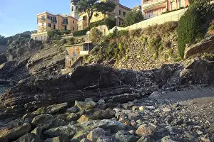 Holiday Maker Prints: Town buildings on a cliff facing the sea at sunset seen from a cove
