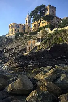 Holiday Maker Prints: Town buildings on a cliff facing the sea at sunset seen from a cove