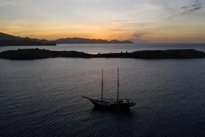 A traditional Pinisi schooner sails at sunset in Komodo National Park, Indonesia. This tropical area is known for its marine biodiversity