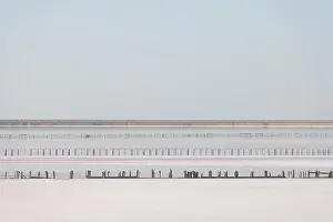 Tranquil minimalist landscape with smooth surface of the pink salt lake with wooden posts with clear sky in sunrise time