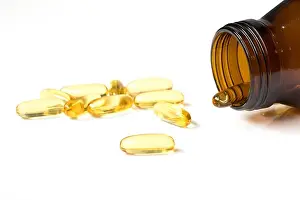 Dietary Prints: Transparent yellow soft gelatin capsule with amber glass bottle on white background