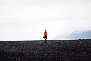 Stone Stream Prints: Traveler in a red jacket standing on a black sand beach in Iceland